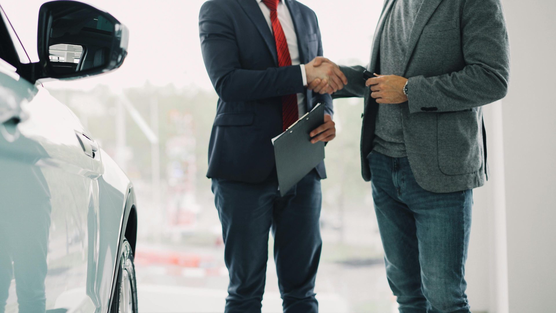 Zwei Männer schütteln sich in einem Autohaus die Hände und signalisieren damit ein Geschäft.