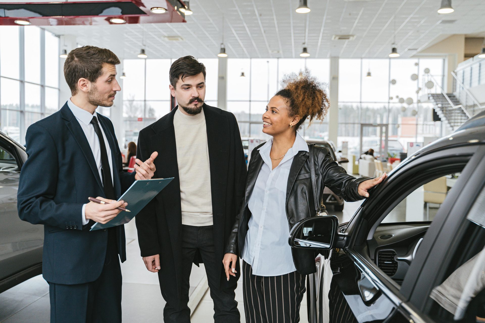 Eine Gruppe Erwachsener unterschiedlicher Herkunft diskutiert im Ausstellungsraum eines Autohauses über den Kauf eines Autos.